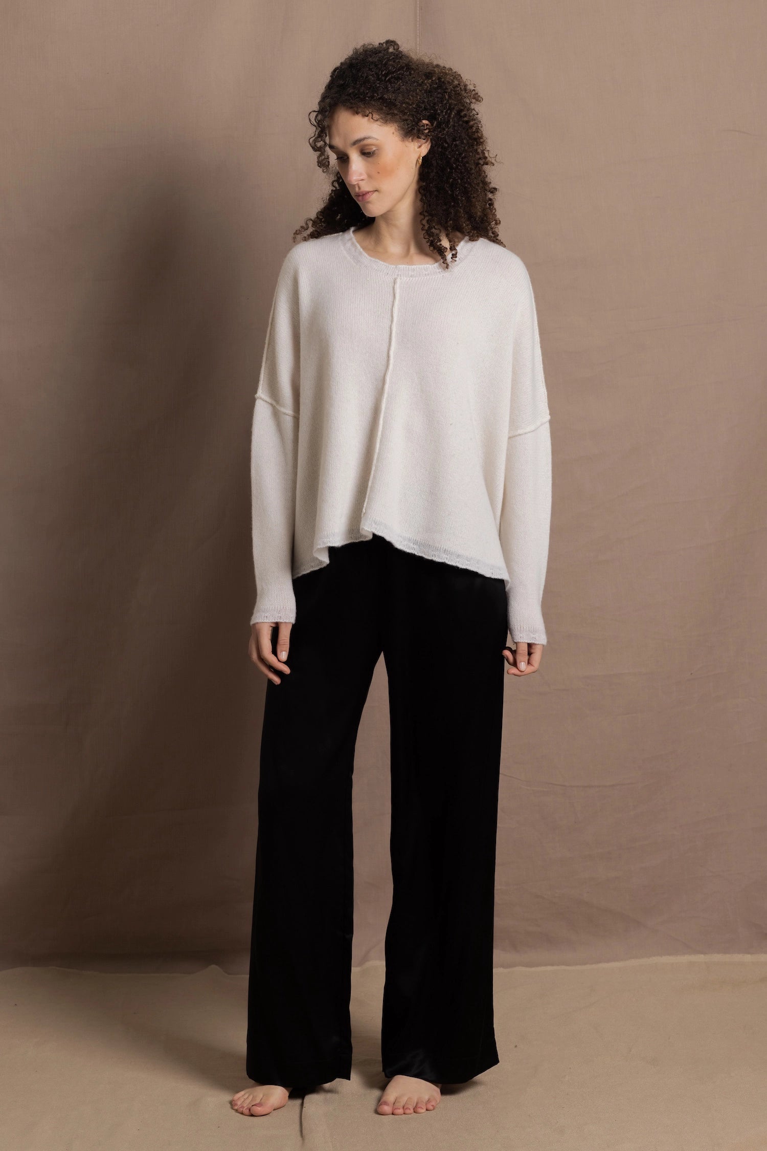 A woman wears an oversized 100% cashmere sweater in Ivory with black silk trousers