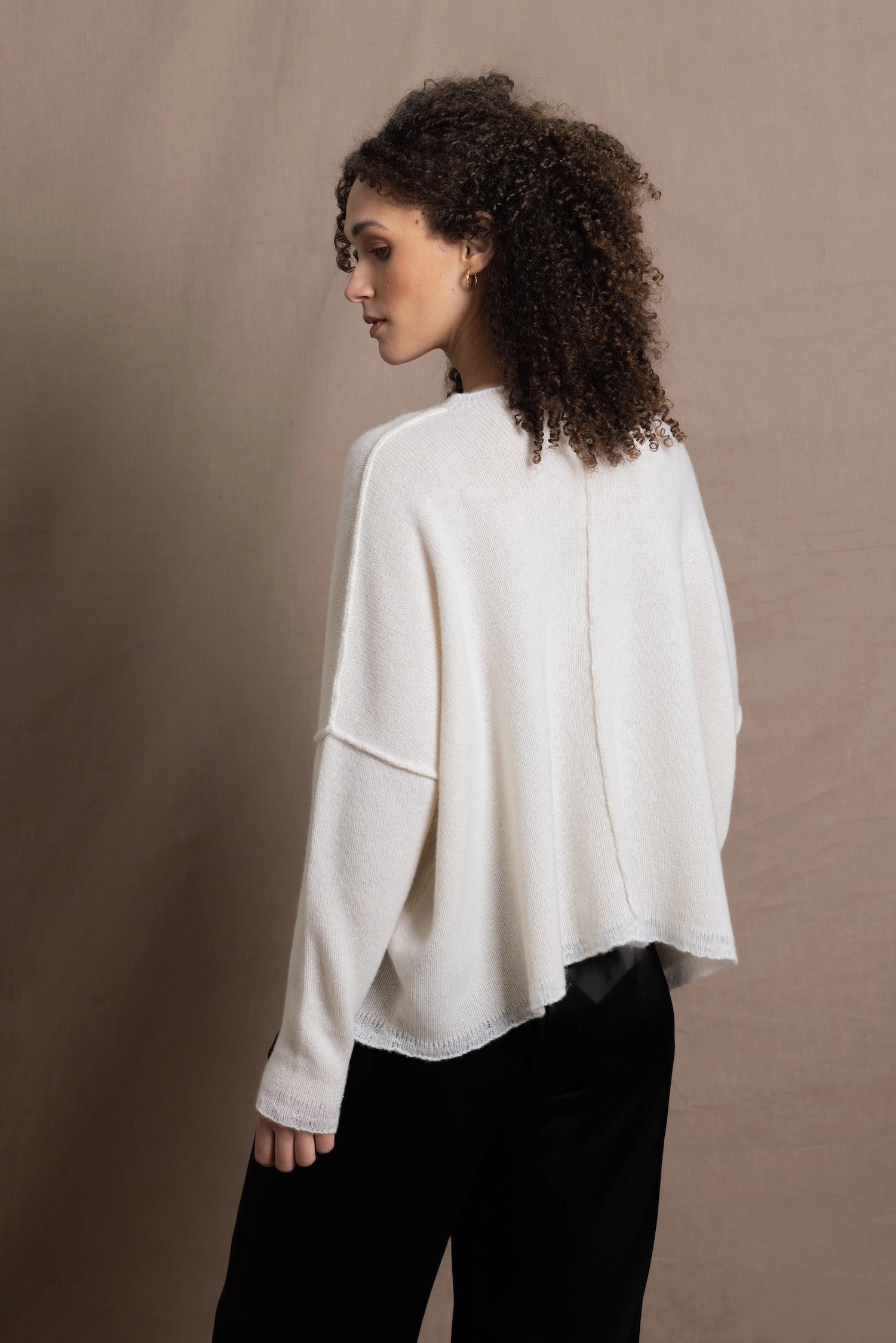 A woman wears an oversized 100% cashmere sweater in Ivory with black silk trousers