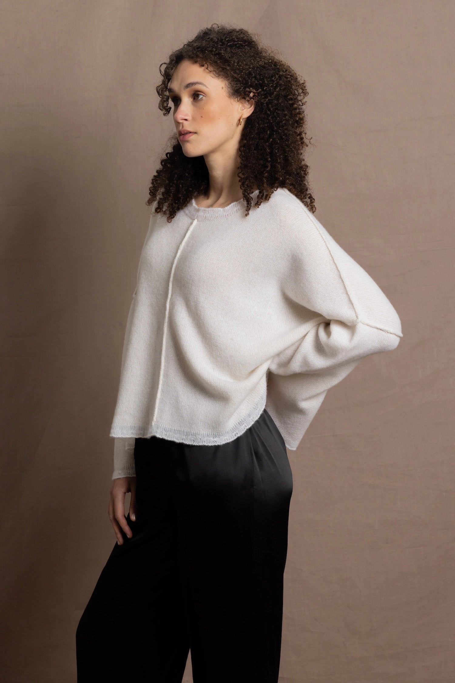 A woman wears an oversized 100% cashmere sweater in Ivory with black silk trousers