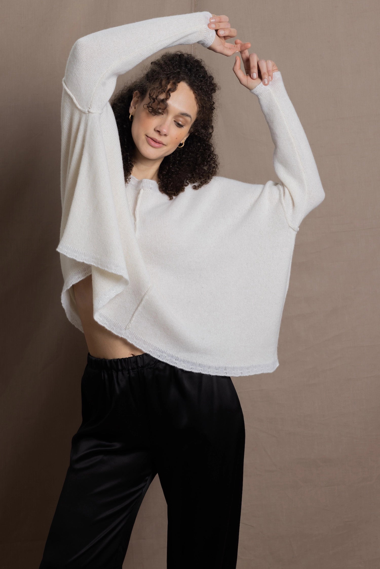 A woman wears an oversized 100% cashmere sweater in Ivory with black silk trousers
