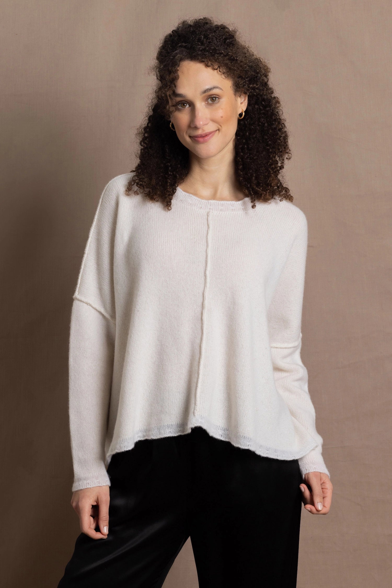 A woman wears an oversized 100% cashmere sweater in Ivory with black silk trousers