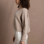 A woman wears a cropped cashmere sweater in beige with white silk shorts