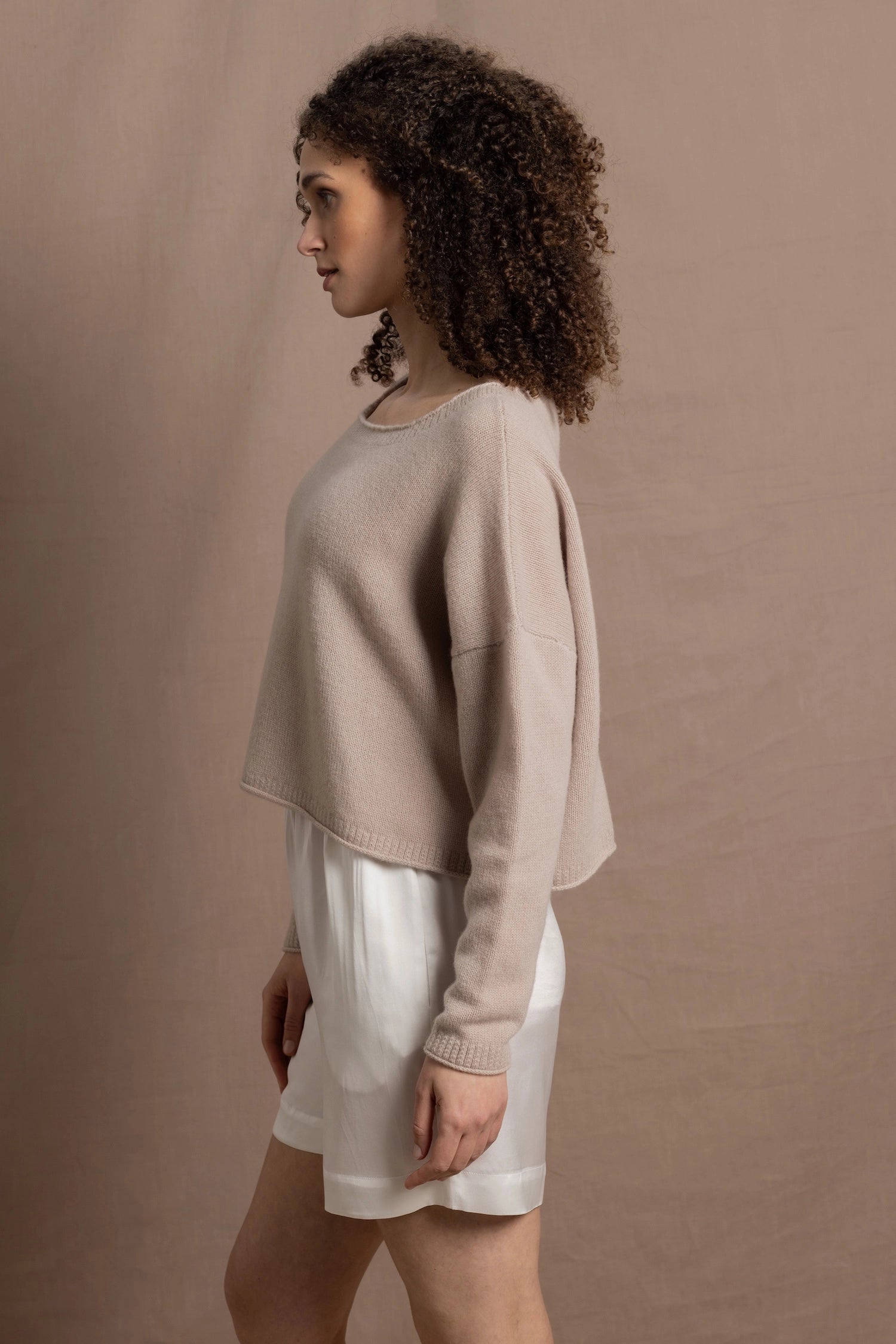 A woman wears a cropped cashmere sweater in beige with white silk shorts