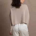 A woman wears a cropped cashmere sweater in beige with white silk shorts