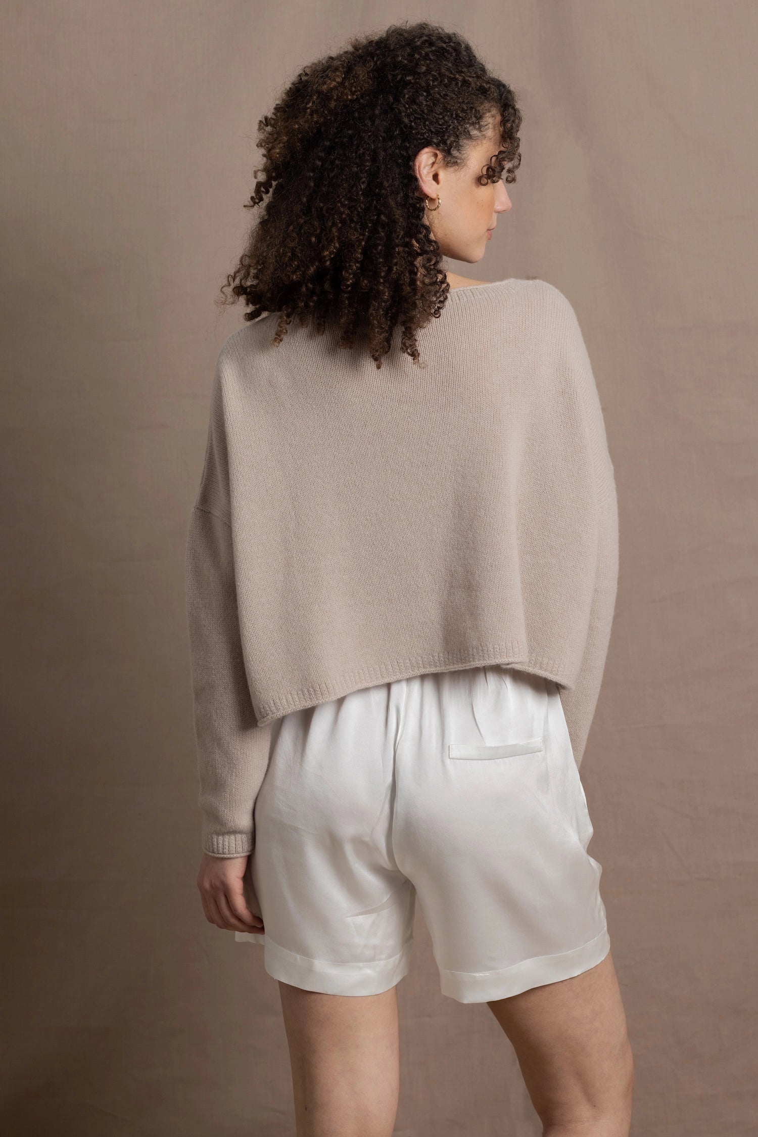 A woman wears a cropped cashmere sweater in beige with white silk shorts