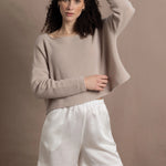 A woman wears a cashmere jumper in beige with white silk shorts