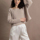 A woman wears a cashmere jumper in beige with white silk shorts