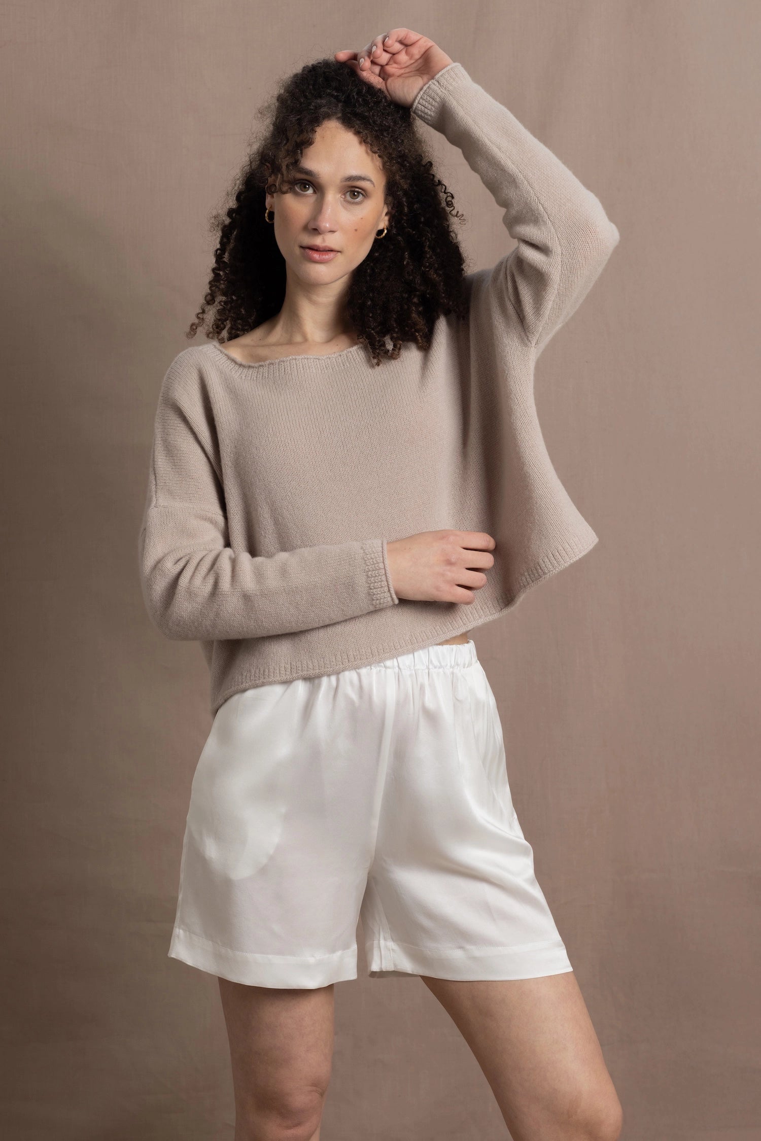 A woman wears a cashmere jumper in beige with white silk shorts