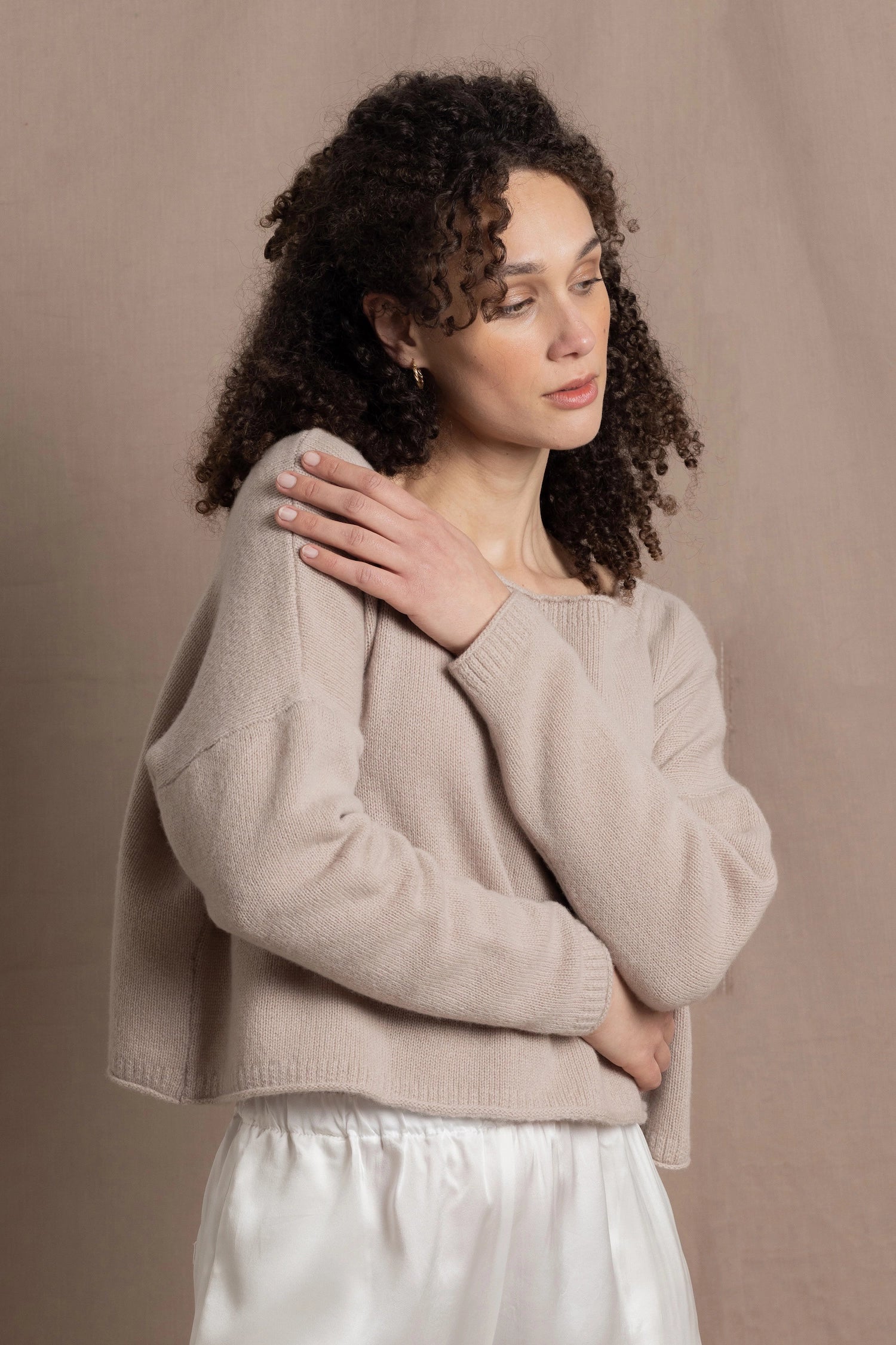 A woman wears a 100% cashmere cropped sweater in beige with white silk shorts