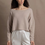 A woman wears a cropped cashmere sweater in beige with white silk shorts