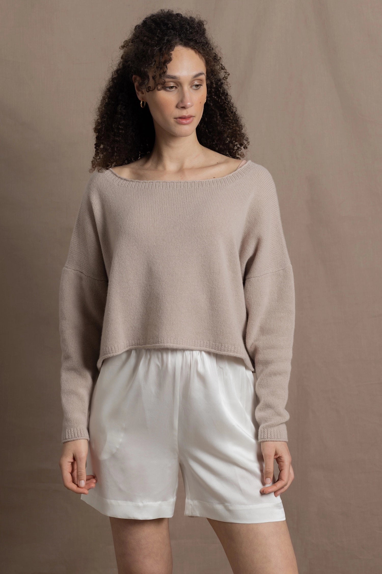 A woman wears a cropped cashmere sweater in beige with white silk shorts