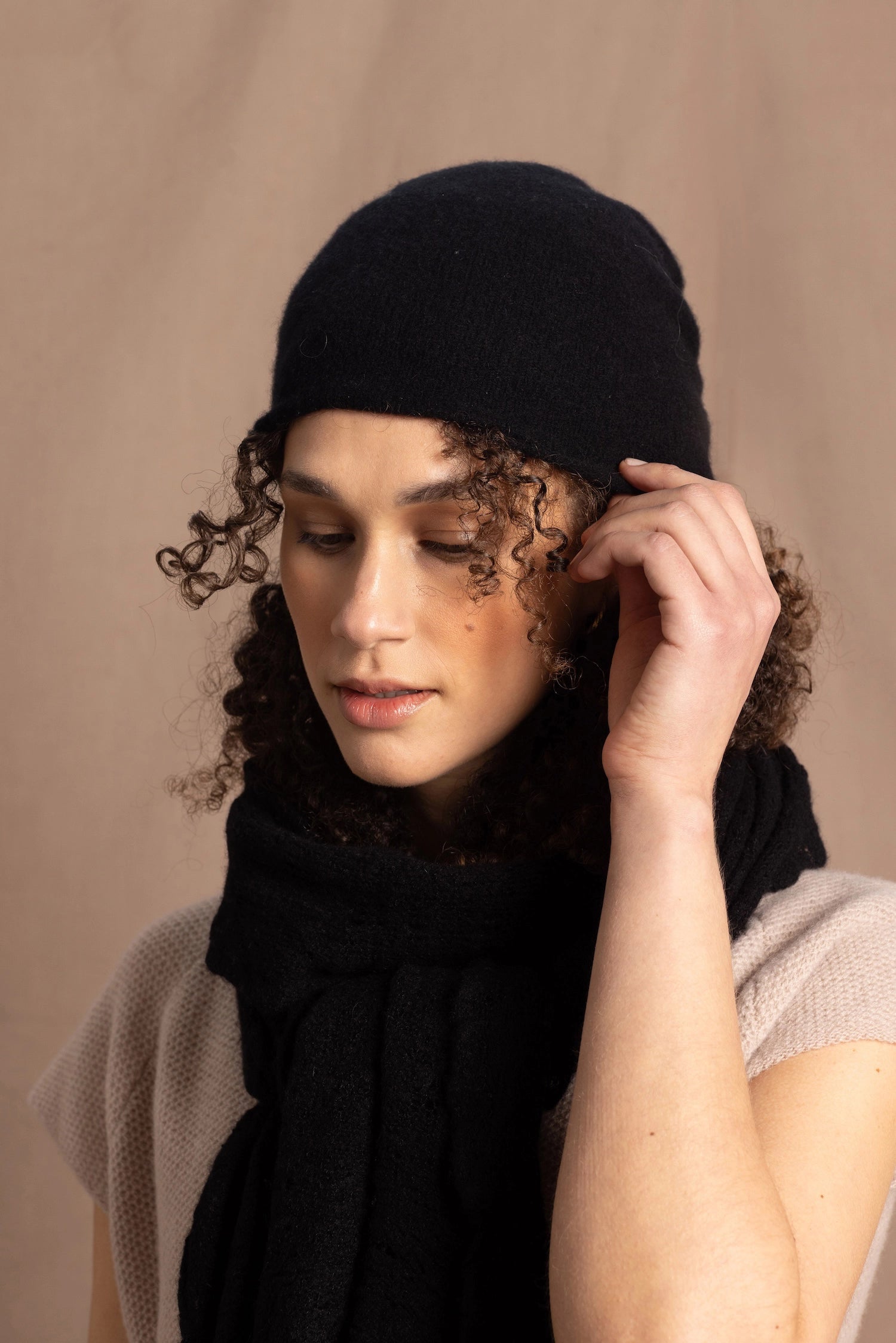 Lady wears luxury cashmere beanie hat in Black with curly hair