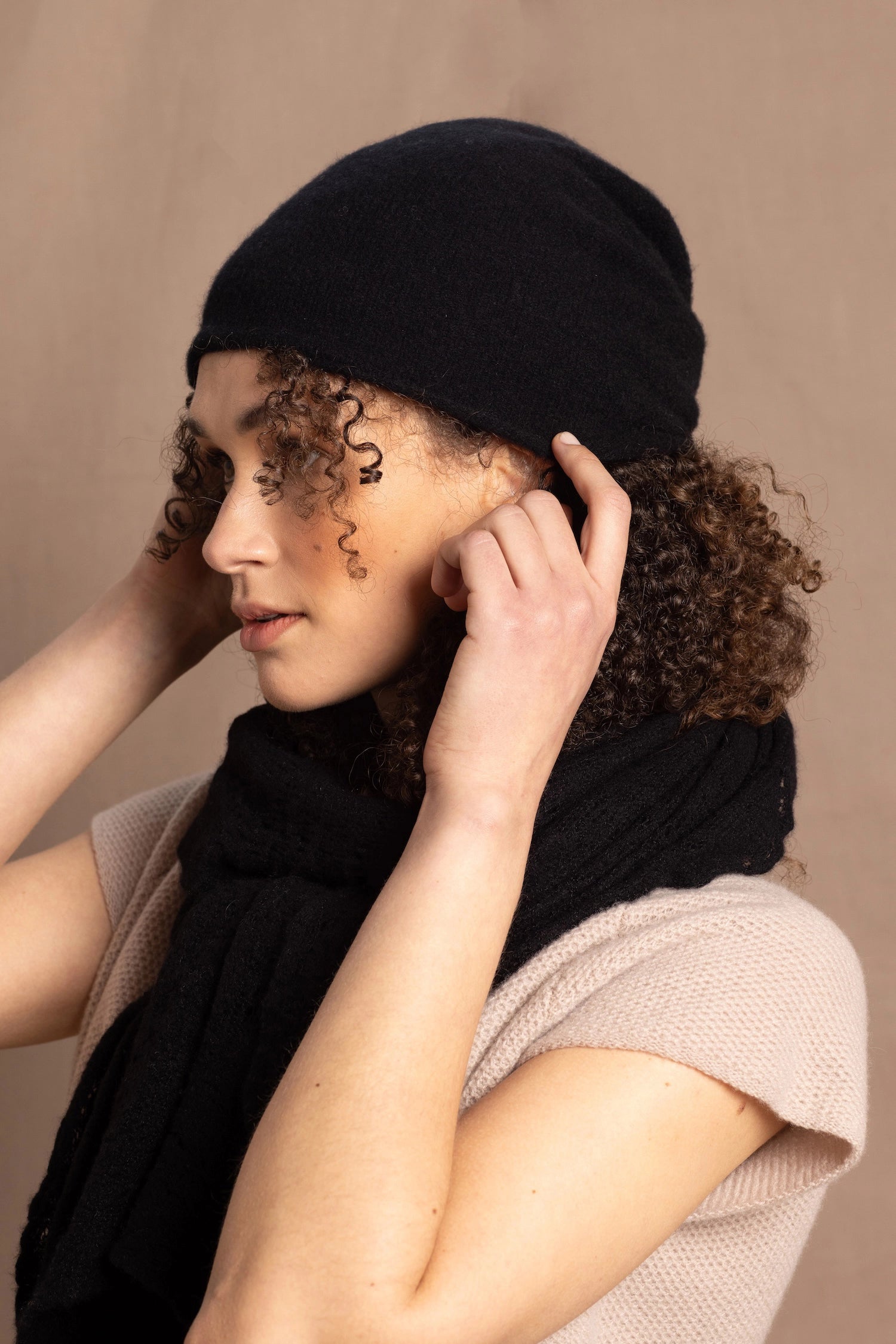 Lady wears luxury cashmere beanie hat in Black with curly hair
