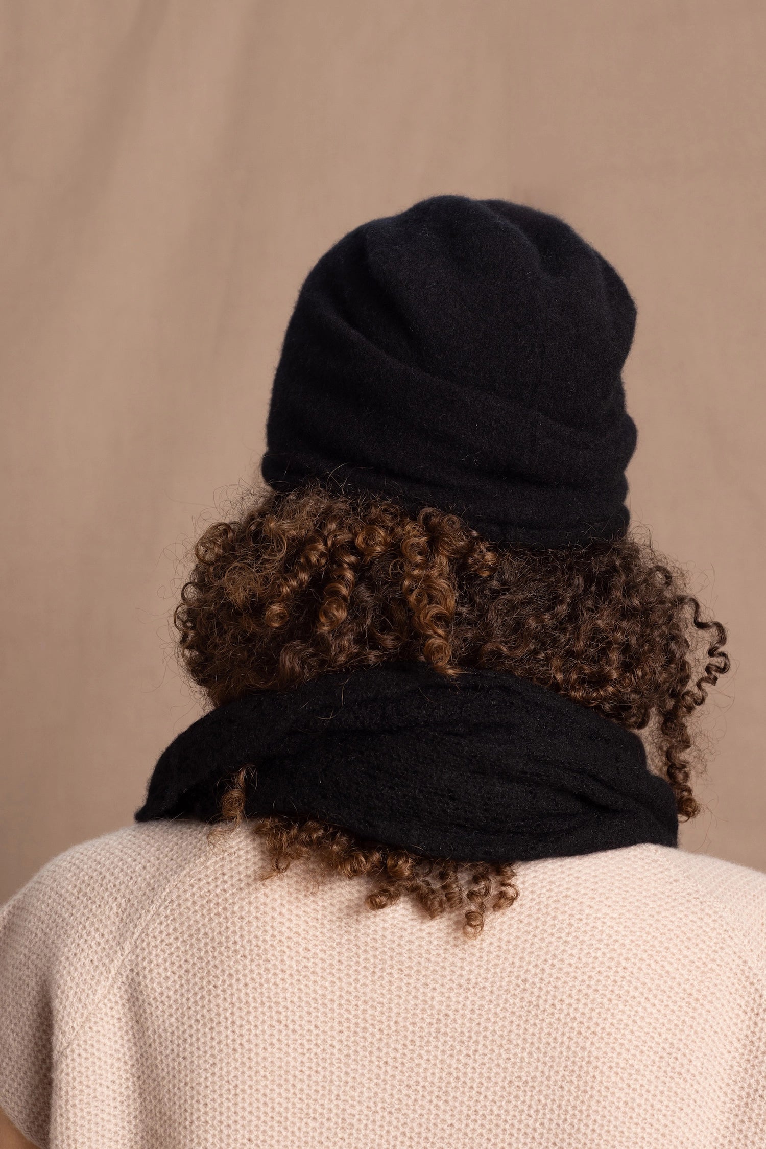 Lady wears luxury cashmere beanie hat in Black with curly hair