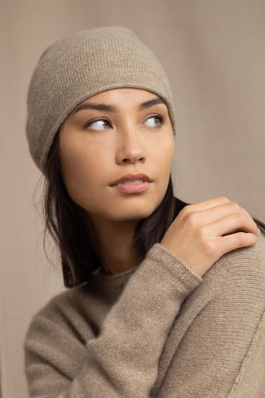 Woman wearing a beige cashmere knit beanie hat with a gold sparkle