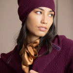 A woman wearing a deep plum burgundy knit cashmere beanie and matching textured cashmere coat by Irish brand Madigan Cashmere