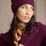 A woman wearing a deep plum burgundy knit cashmere beanie and matching textured cashmere coat by Irish brand Madigan Cashmere