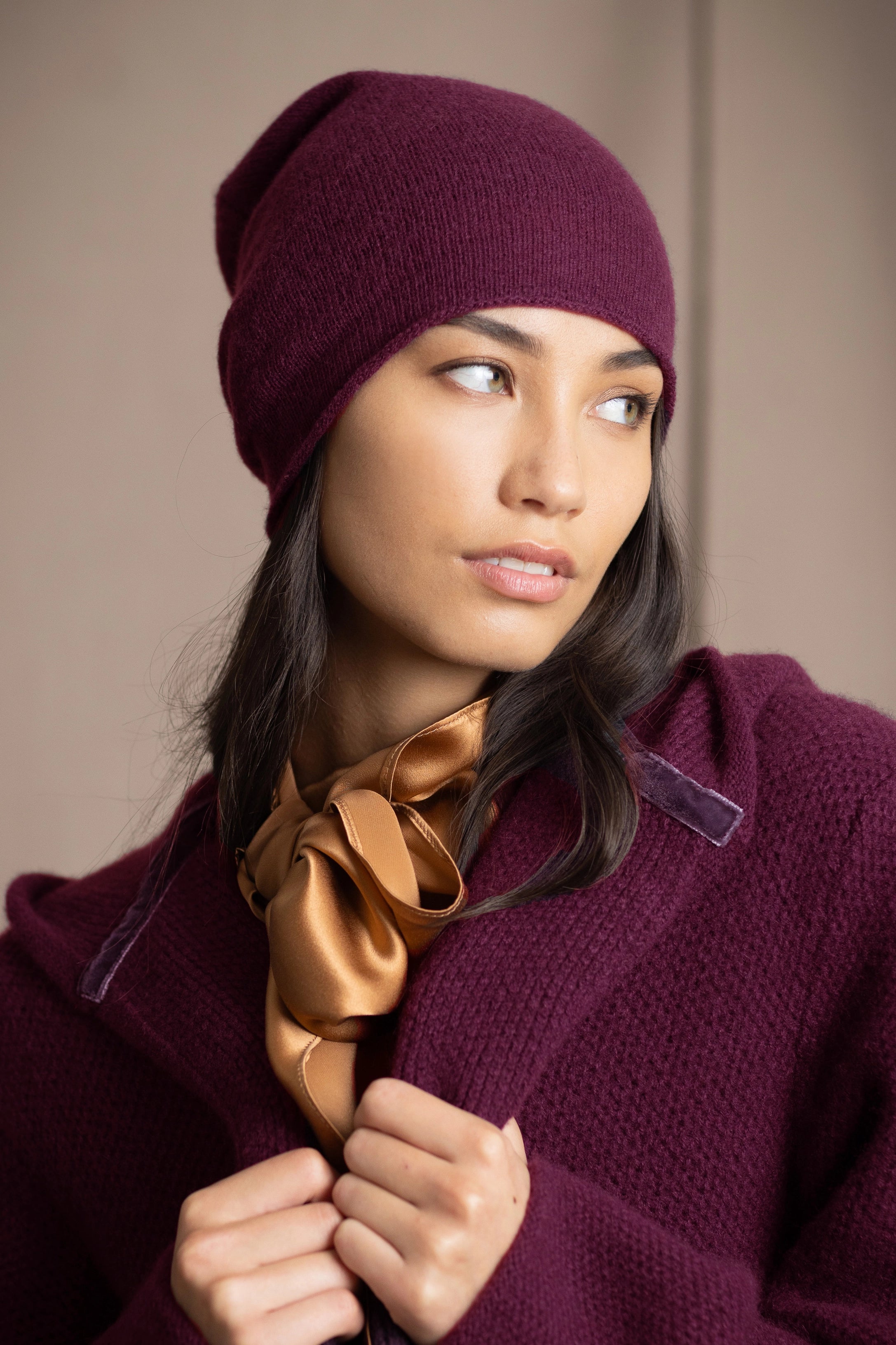 A woman wearing a deep plum burgundy knit cashmere beanie and matching textured cashmere coat by Irish brand Madigan Cashmere