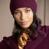 A woman wearing a deep plum burgundy knit cashmere beanie and matching textured cashmere coat by Irish brand Madigan Cashmere