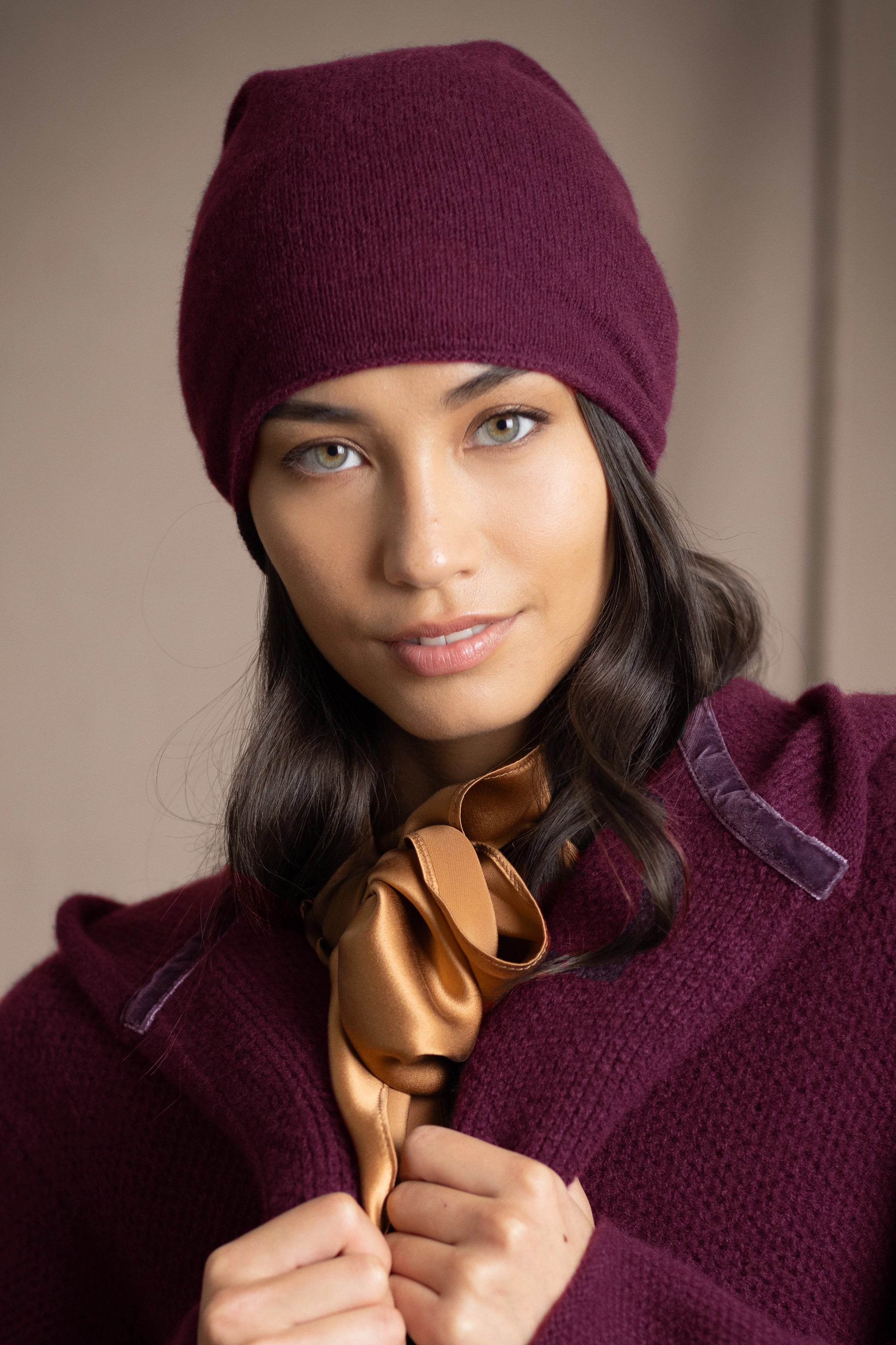 A woman wearing a deep plum burgundy knit cashmere beanie and matching textured cashmere coat by Irish brand Madigan Cashmere