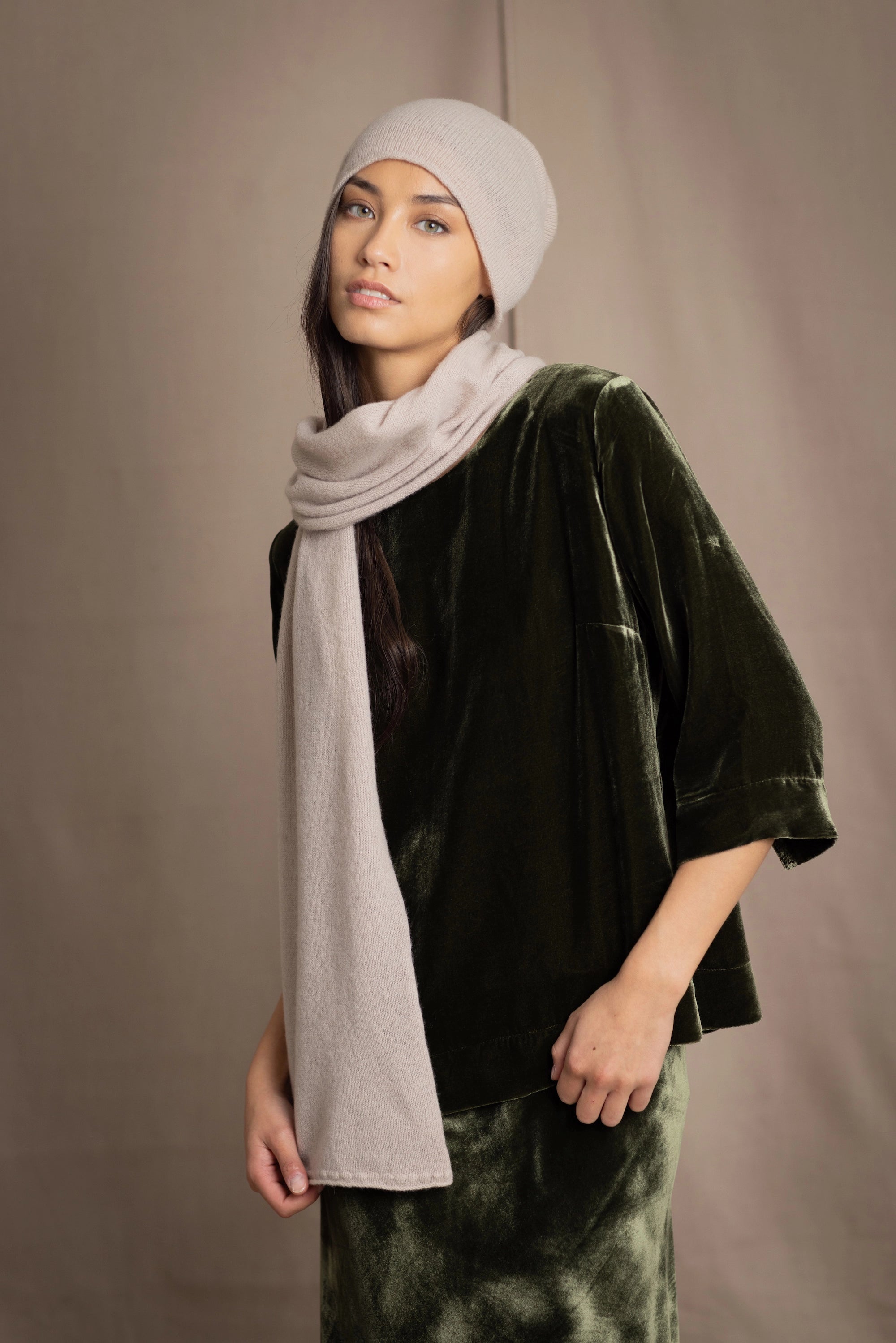 a woman wears a cashmere scarf in beige with matching cashmere beanie hat over silk velvet clothing in olive green