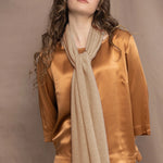 a woman wears a beige sand coloured cashmere scarf over bronze silk clothing