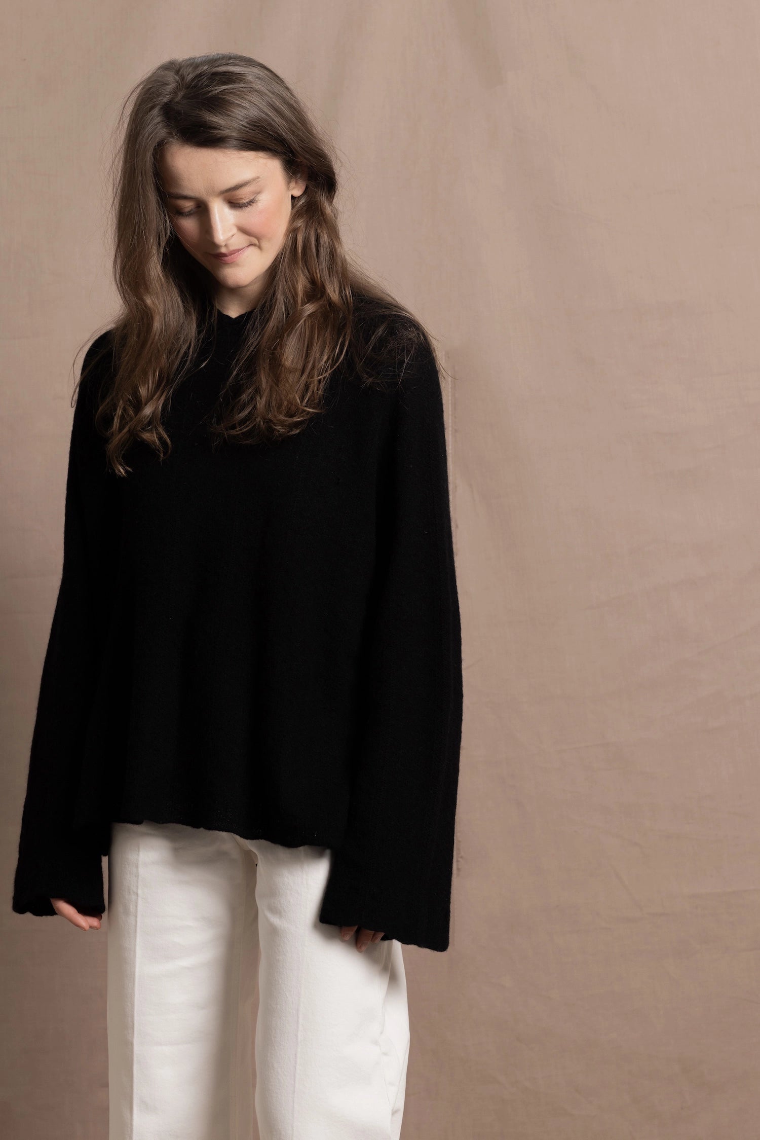 A woman wears an oversized 100% cashmere hooded sweater in black over white jeans