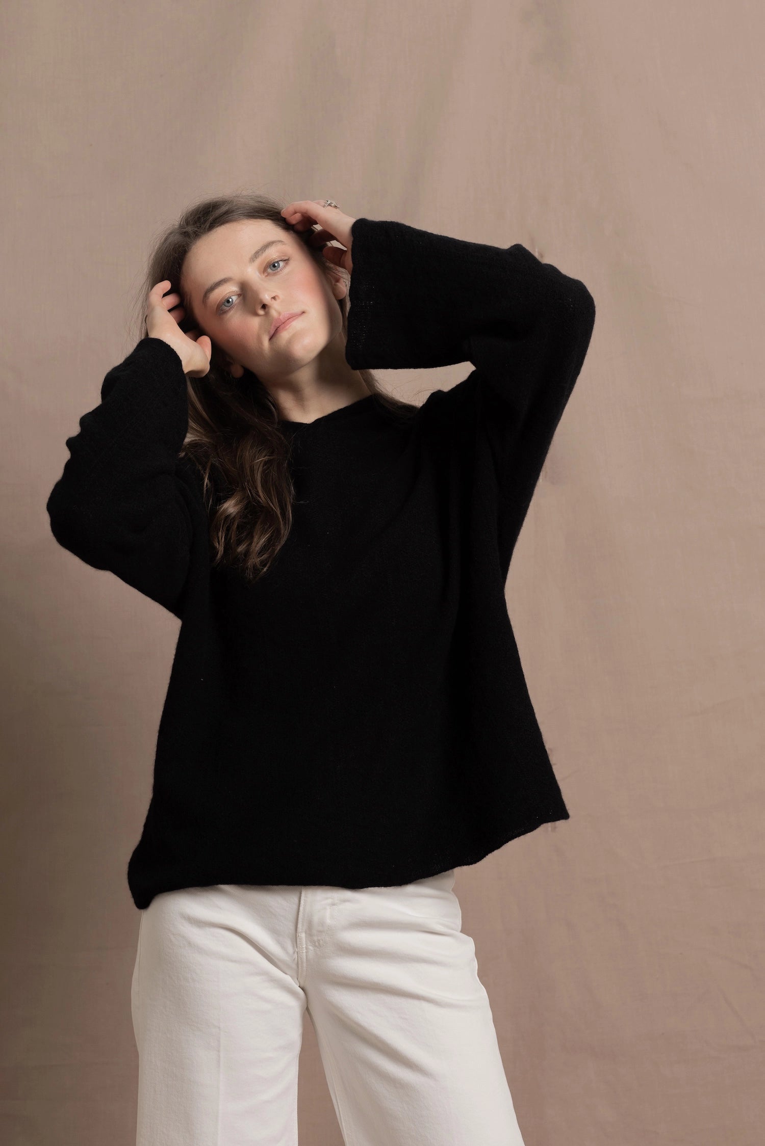 A woman wears an oversized 100% cashmere hoodie in black over white jeans