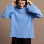 A woman wears a bright cerulean blue cashmere hoodie sweater with black silk shorts