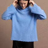 A woman wears a bright cerulean blue cashmere hoodie sweater with black silk shorts