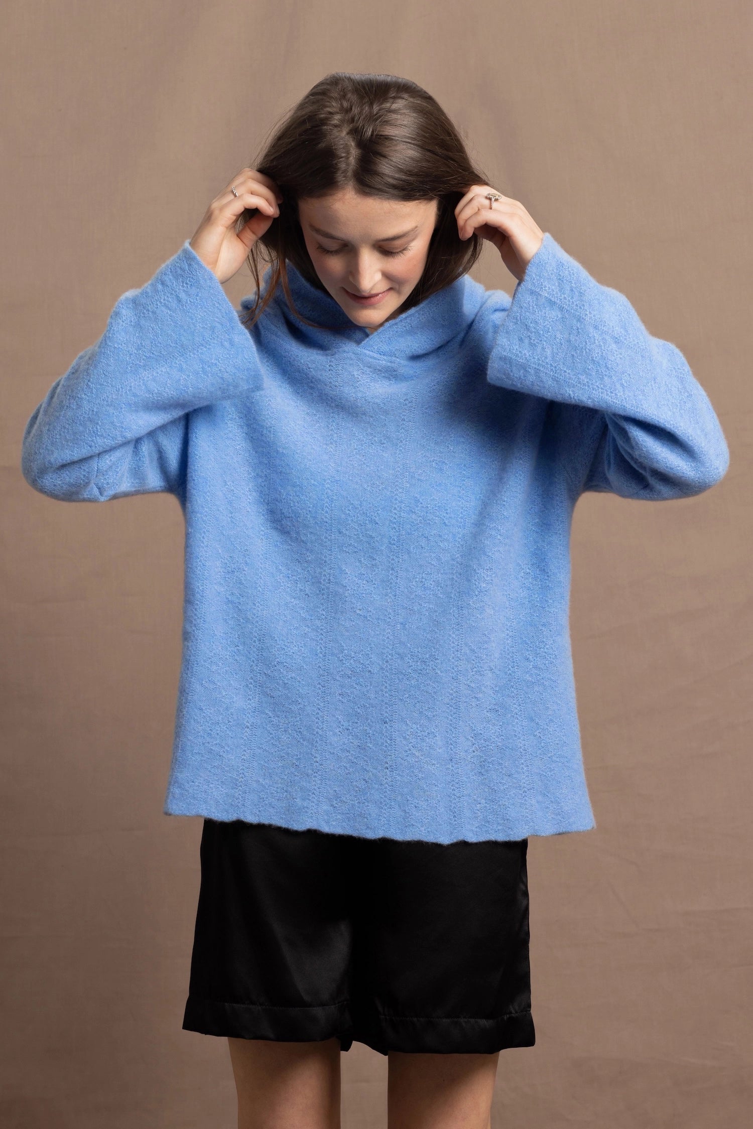 A woman wears a bright cerulean blue cashmere hoodie sweater with black silk shorts