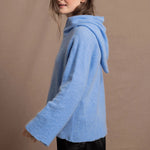 A woman wears a pure 100% cashmere hoodie sweater in blue with black silk shorts