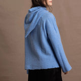 A woman wears a pure 100% cashmere hooded jumper in blue with black silk shorts
