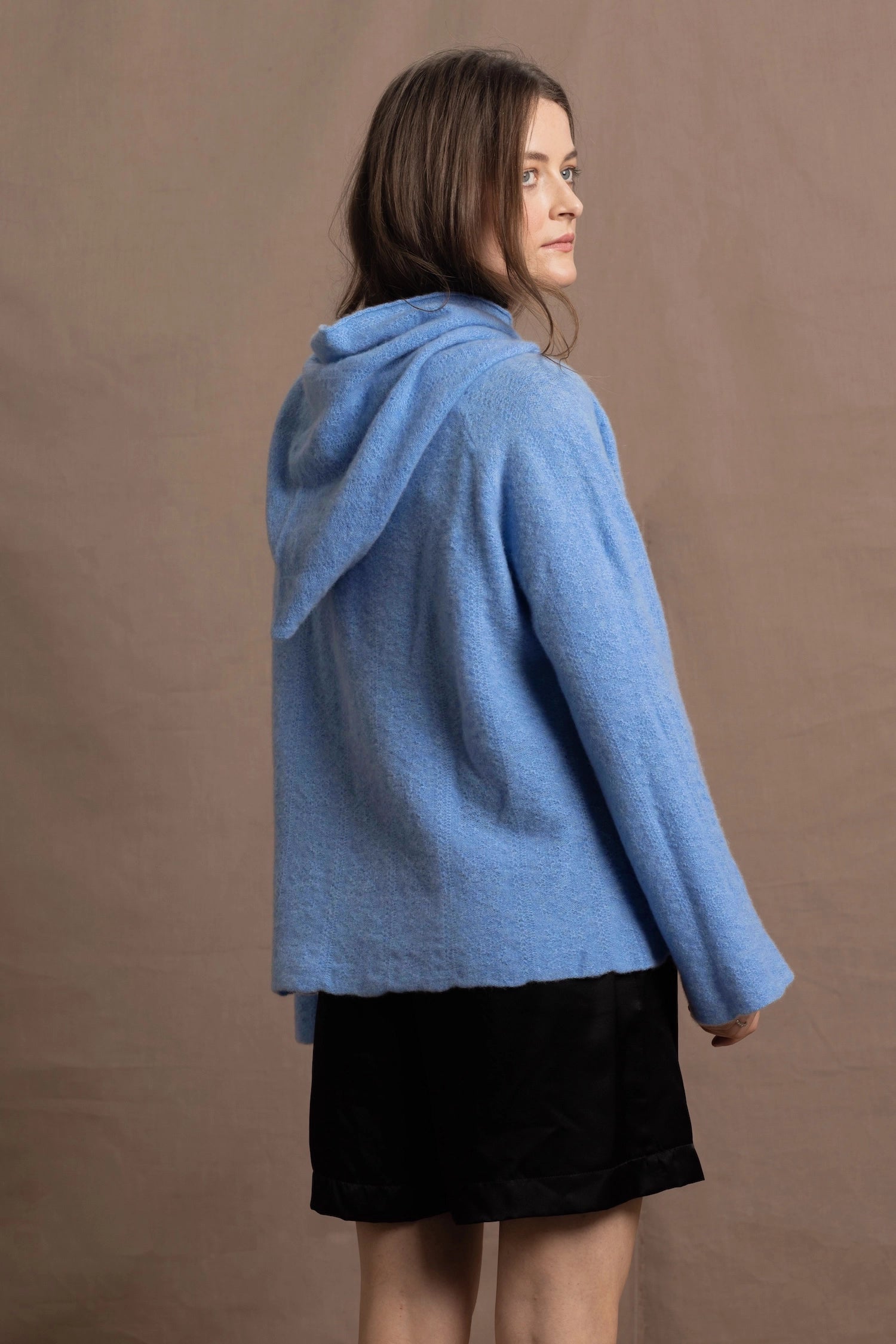 A woman wears a pure 100% cashmere hooded jumper in blue with black silk shorts