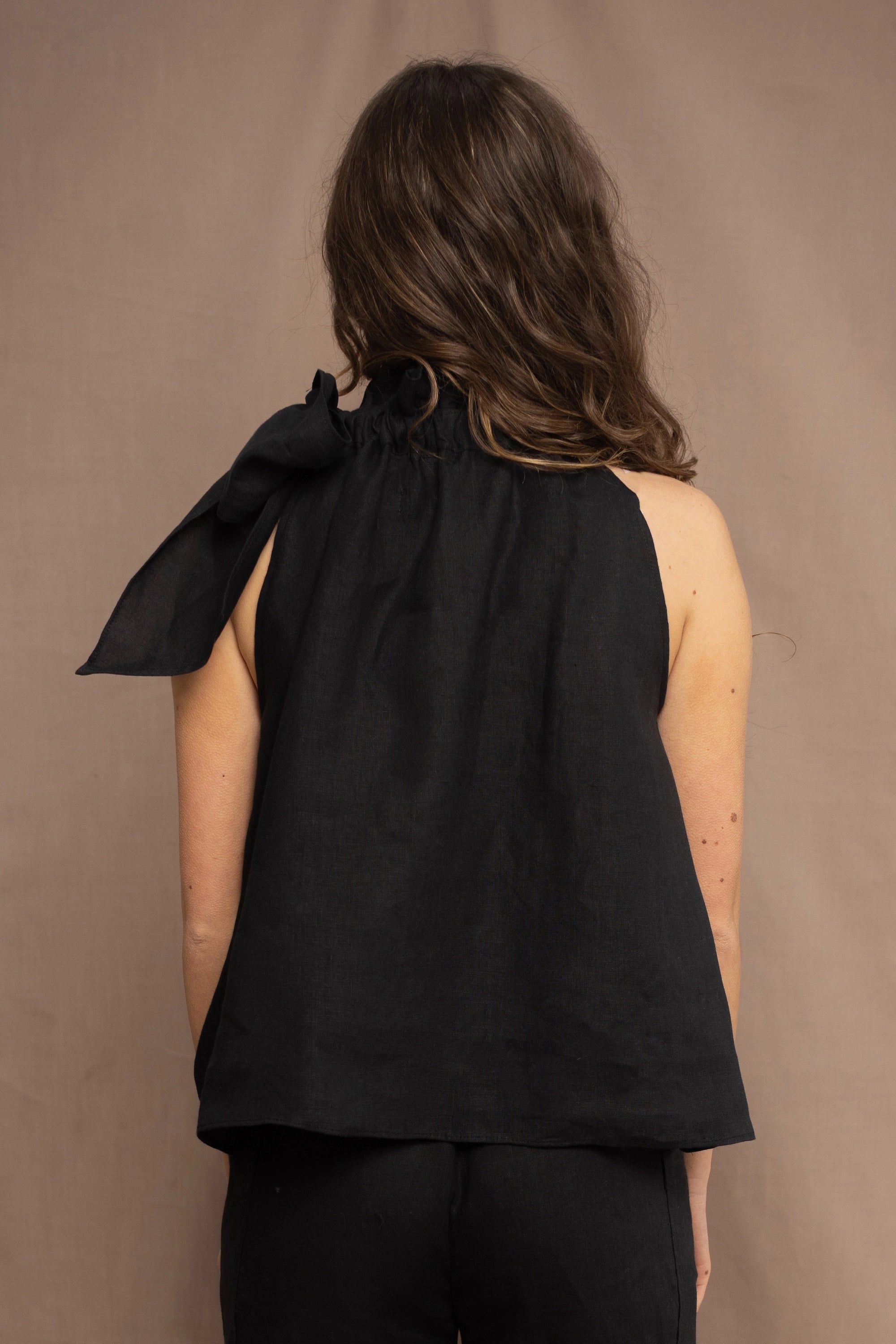a woman wearing an Irish linen halter top with a bow detail around the neck in black with matching linen trousers by Irish brand Madigan