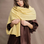 a woman wears a banana yellow cashmere wrap shawl over a ruffled silk blouse top in chocolate brown with matching trousers 