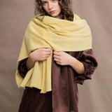 a woman wears a banana yellow cashmere wrap shawl over a ruffled silk blouse top in chocolate brown with matching trousers 