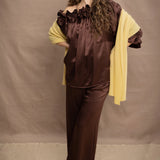 a woman wears a banana yellow cashmere wrap shawl over a ruffled silk blouse top in chocolate brown with matching trousers 