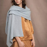 a woman wears a light pale blue turquoise cashmere wrap scarf over bronze silk clothing