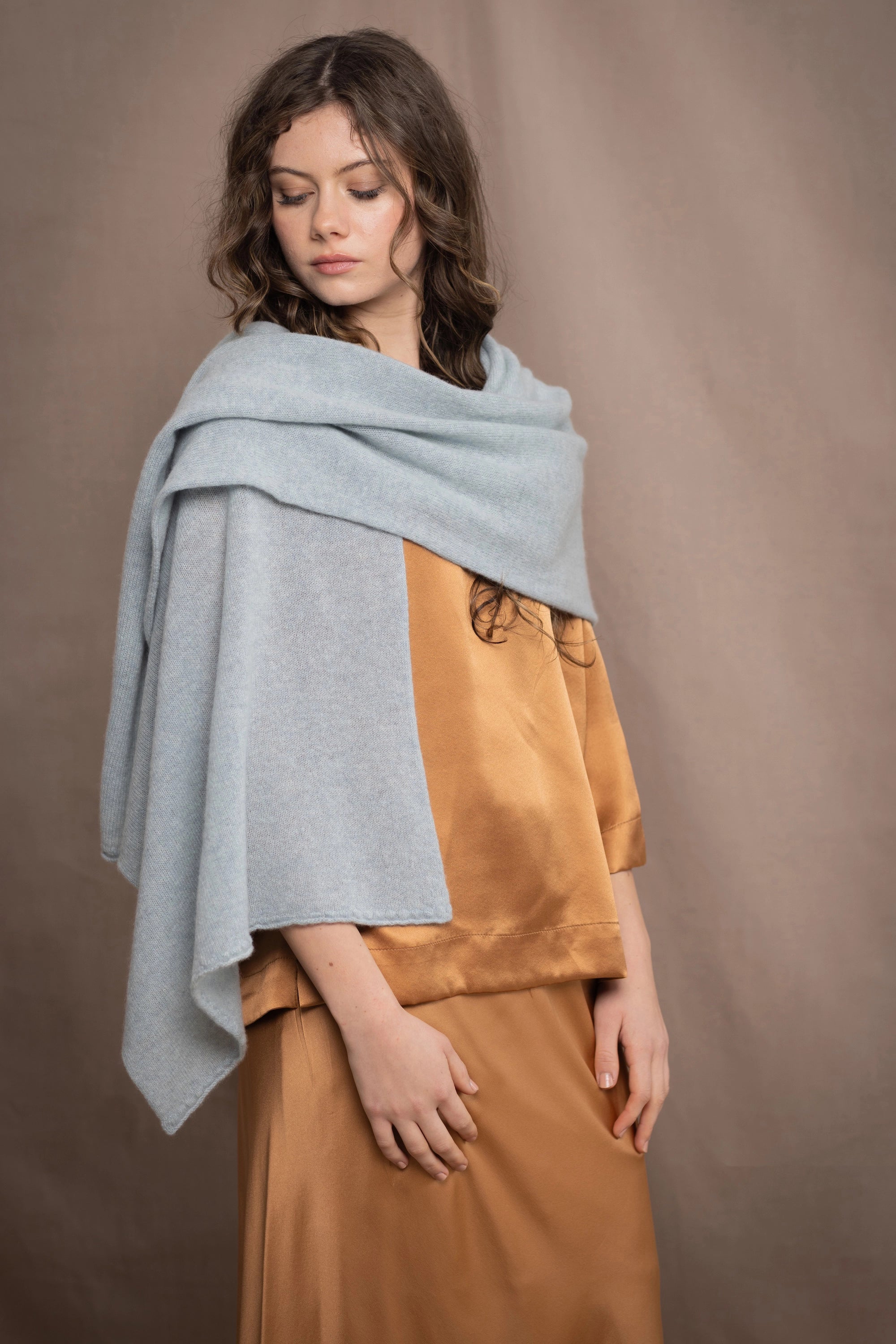 a woman wears a light pale blue turquoise cashmere wrap scarf over bronze silk clothing
