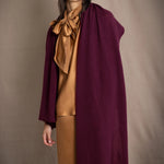 A woman wearing a long, draped plum purple cashmere wrap over bronze silk clothing by Irish brand Madigan Cashmere
