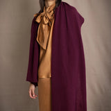 A woman wearing a long, draped plum purple cashmere wrap over bronze silk clothing by Irish brand Madigan Cashmere