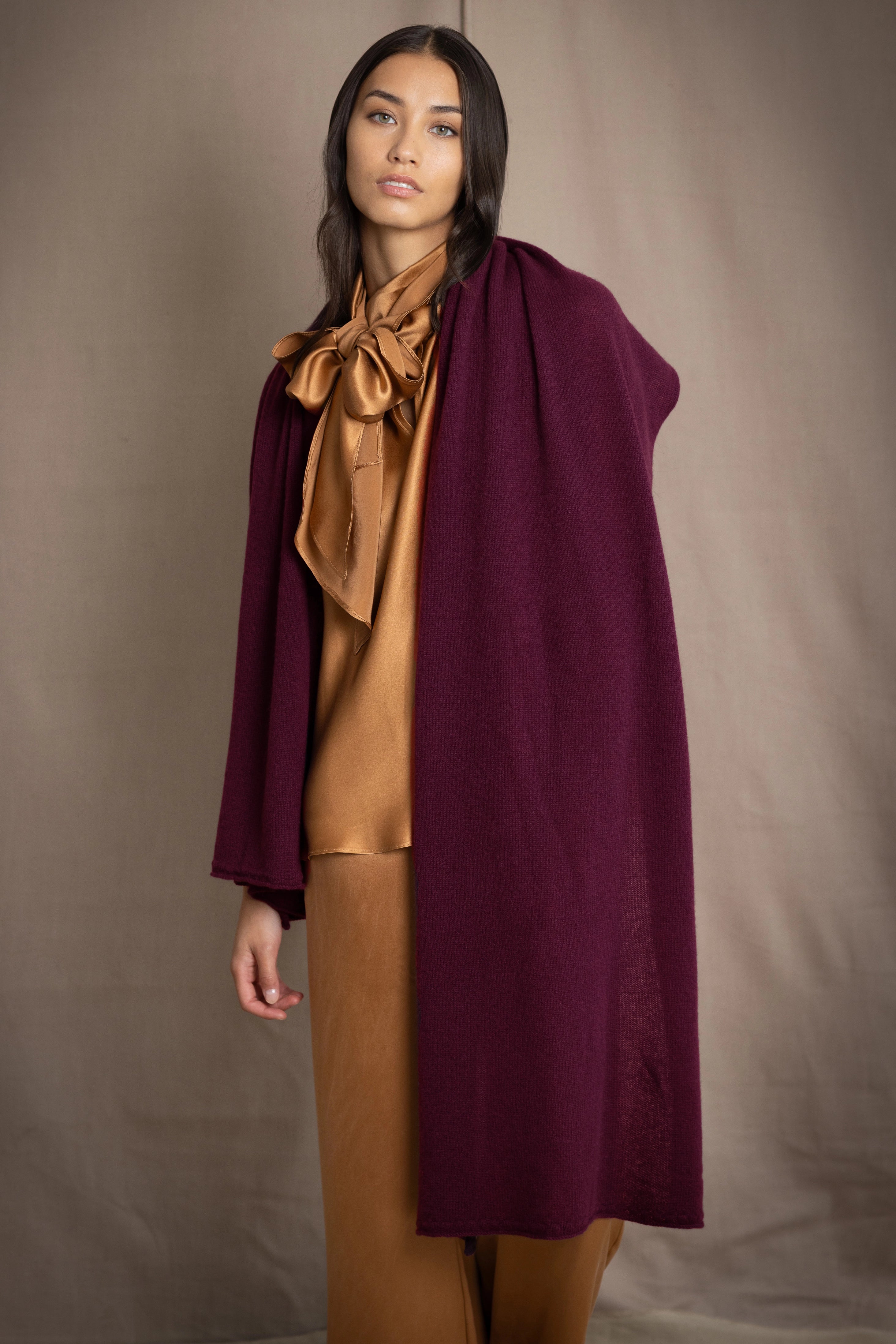 A woman wearing a long, draped plum purple cashmere wrap over bronze silk clothing by Irish brand Madigan Cashmere