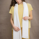 a woman wears a mid sized cashmere scarf in white by Irish brand Madigan Cashmere over yellow cashmere tee and silk trousers in yellow