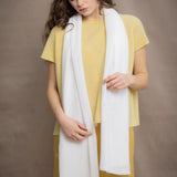 a woman wears a mid sized cashmere scarf in white by Irish brand Madigan Cashmere over yellow cashmere tee and silk trousers in yellow