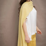 a woman wears a banana yellow cashmere wrap shawl over a white silk top and yellow silk trousers
