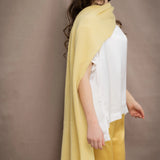 a woman wears a banana yellow cashmere wrap shawl over a white silk top and yellow silk trousers