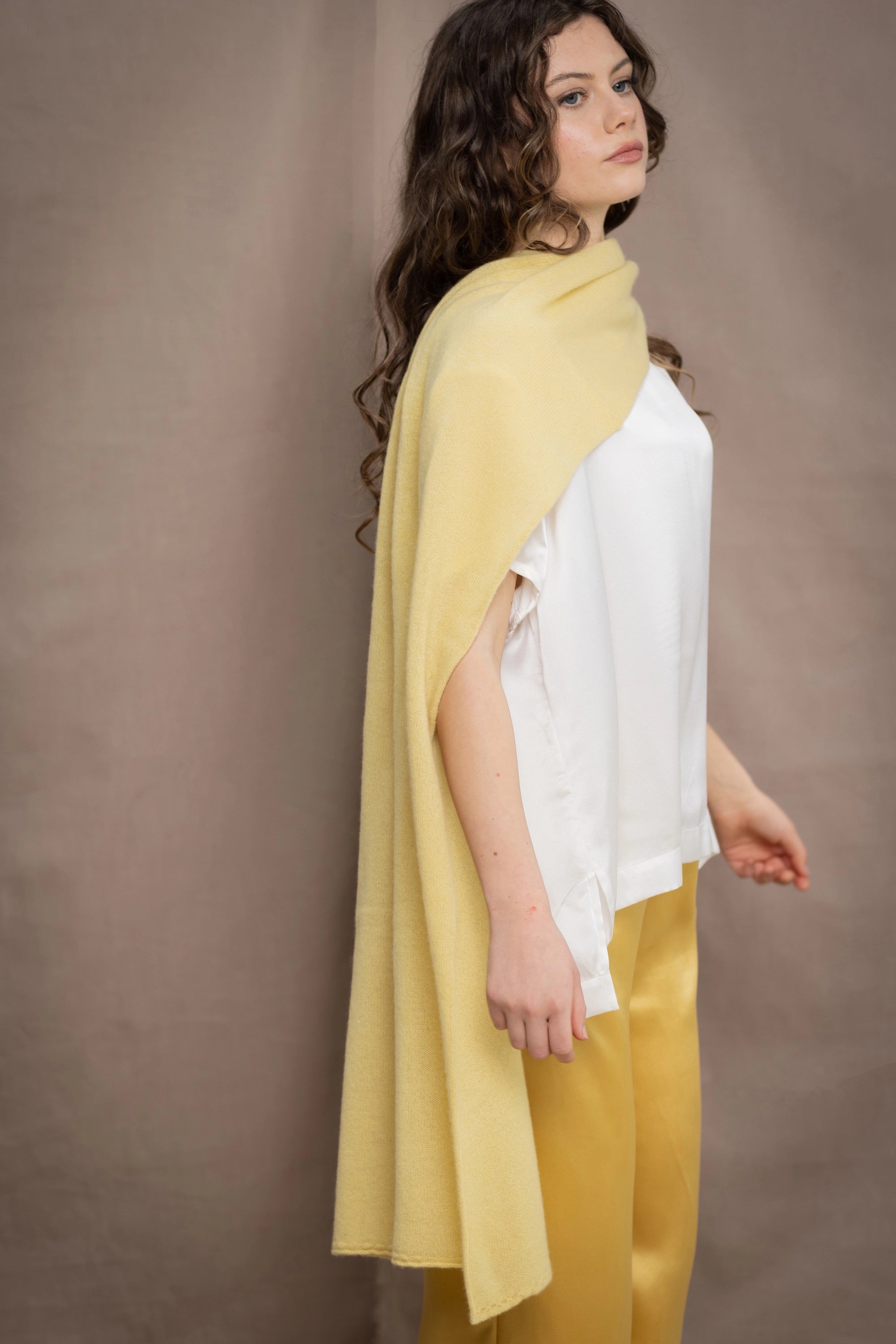 a woman wears a banana yellow cashmere wrap shawl over a white silk top and yellow silk trousers