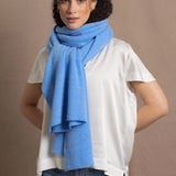 a woman wears a cerulean blue wrap scarf tied around her neck and paired with a silk white tee and jeans