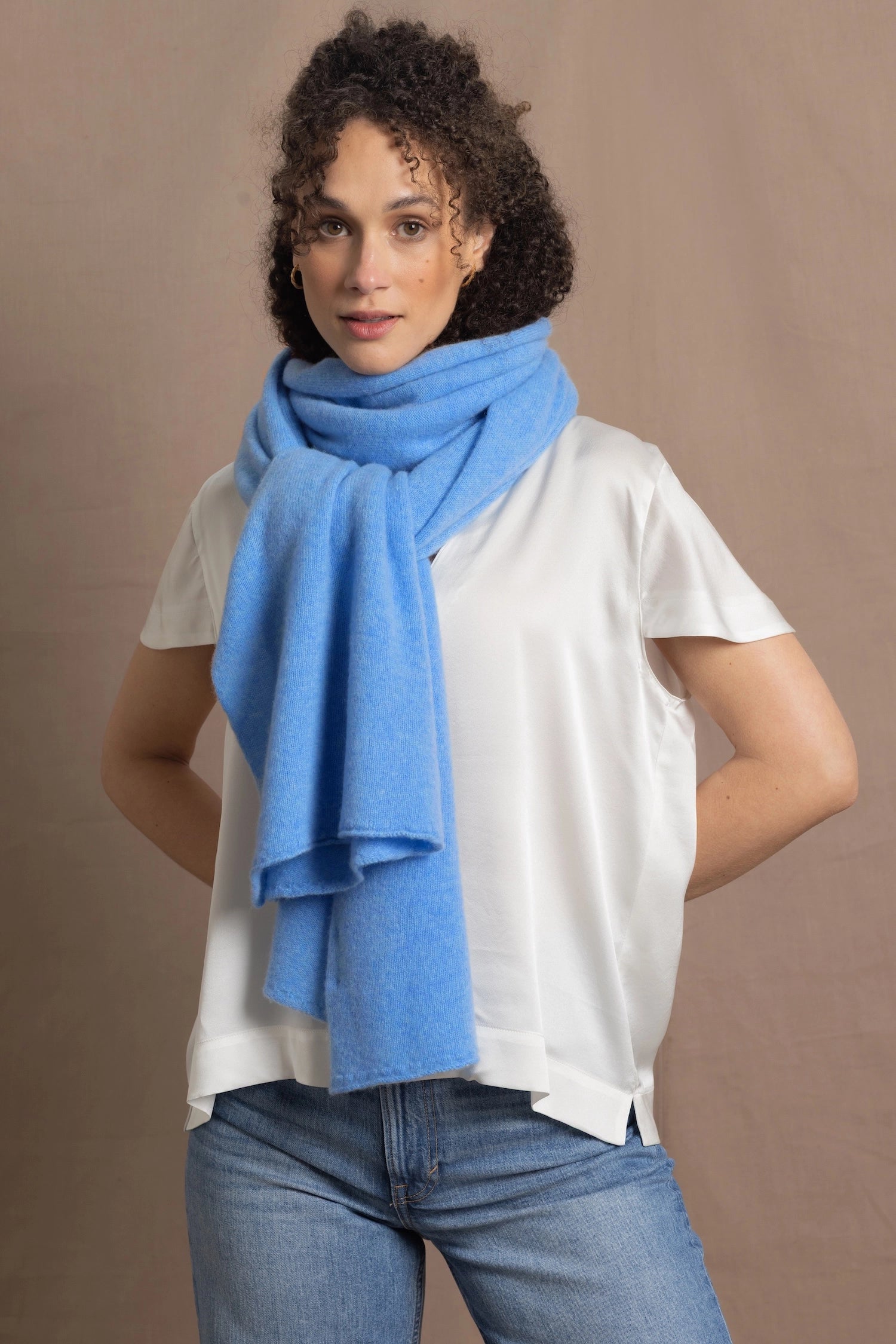 a woman wears a cerulean blue wrap scarf tied around her neck and paired with a silk white tee and jeans